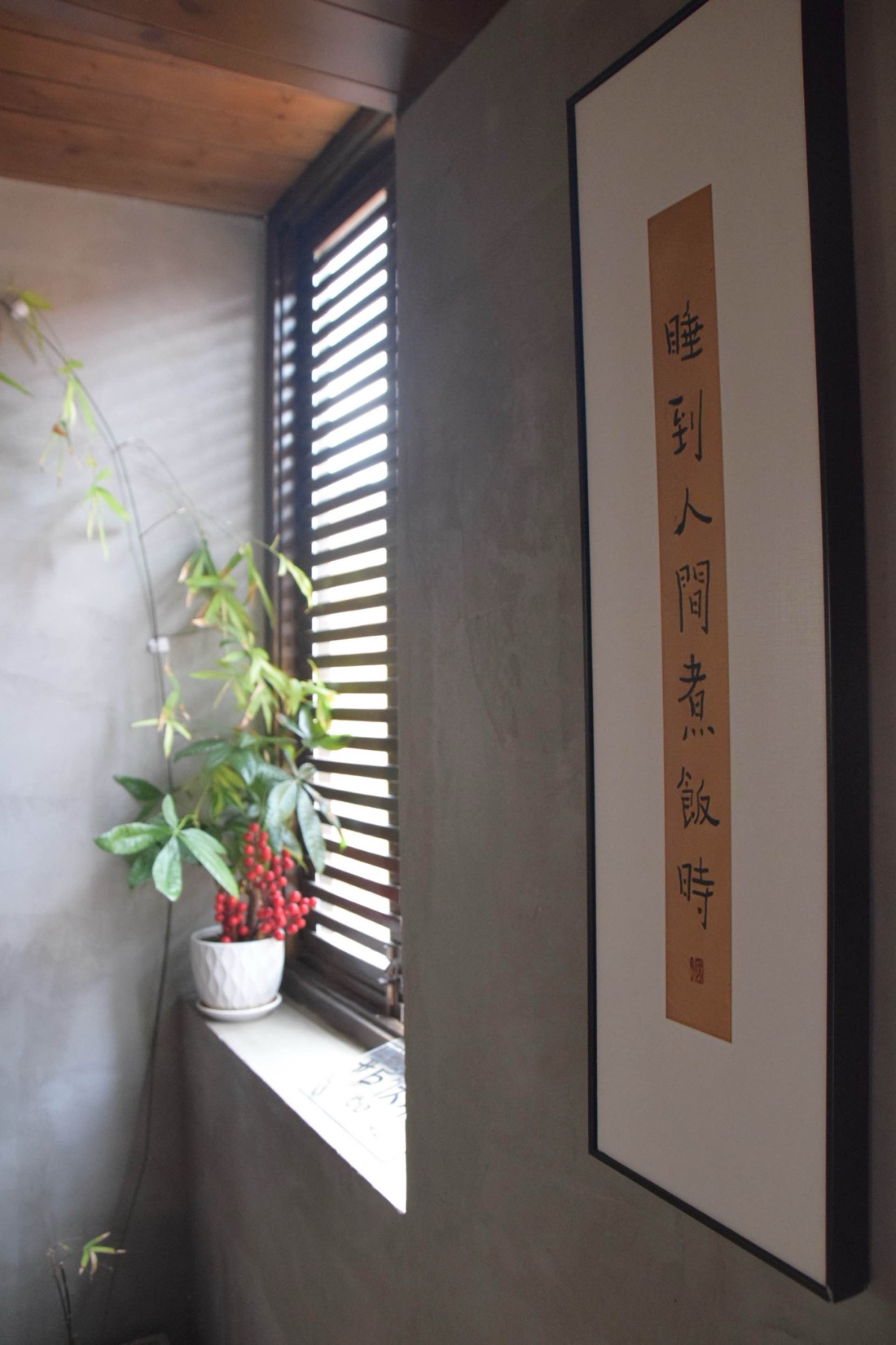 A framed calligraphy scroll beside a window with plants